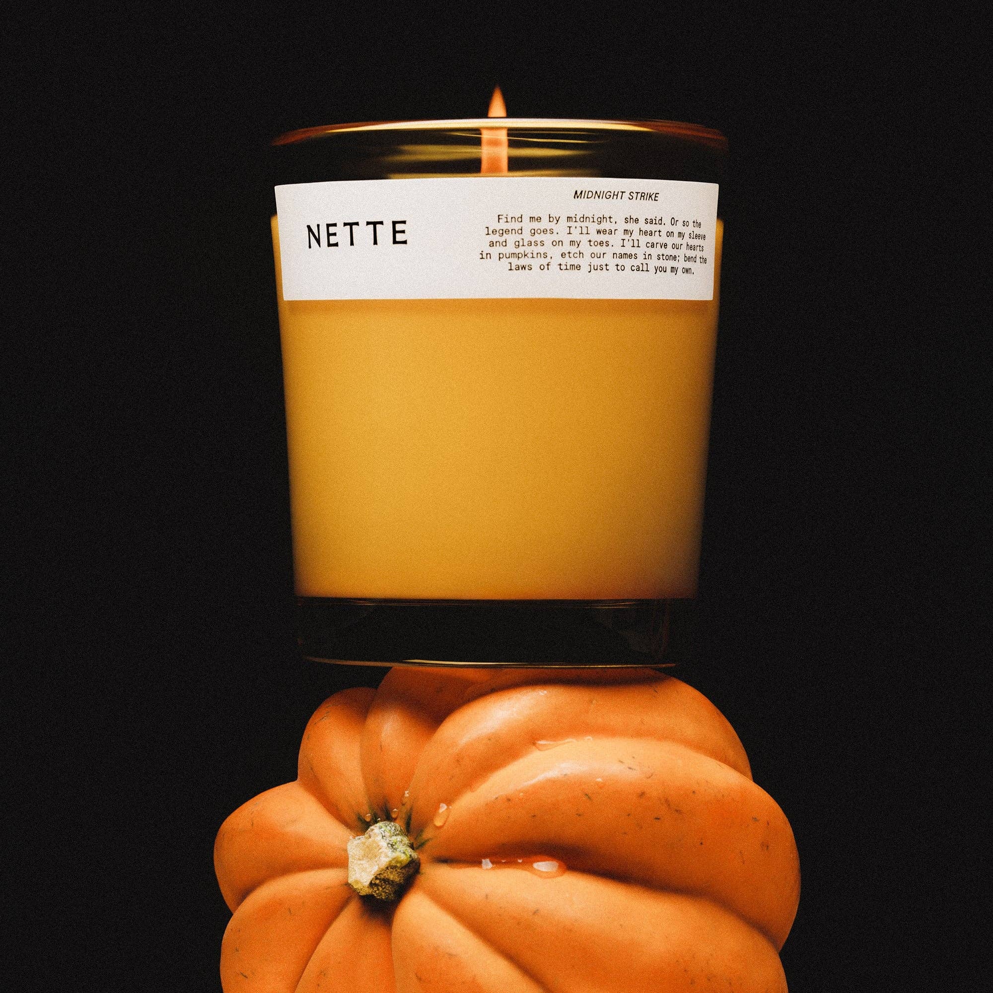 Candle labeled 'NETTE' on a small pumpkin against a black background