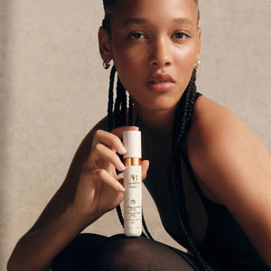 Woman holding an Augustinus Bader skincare product with a neutral background