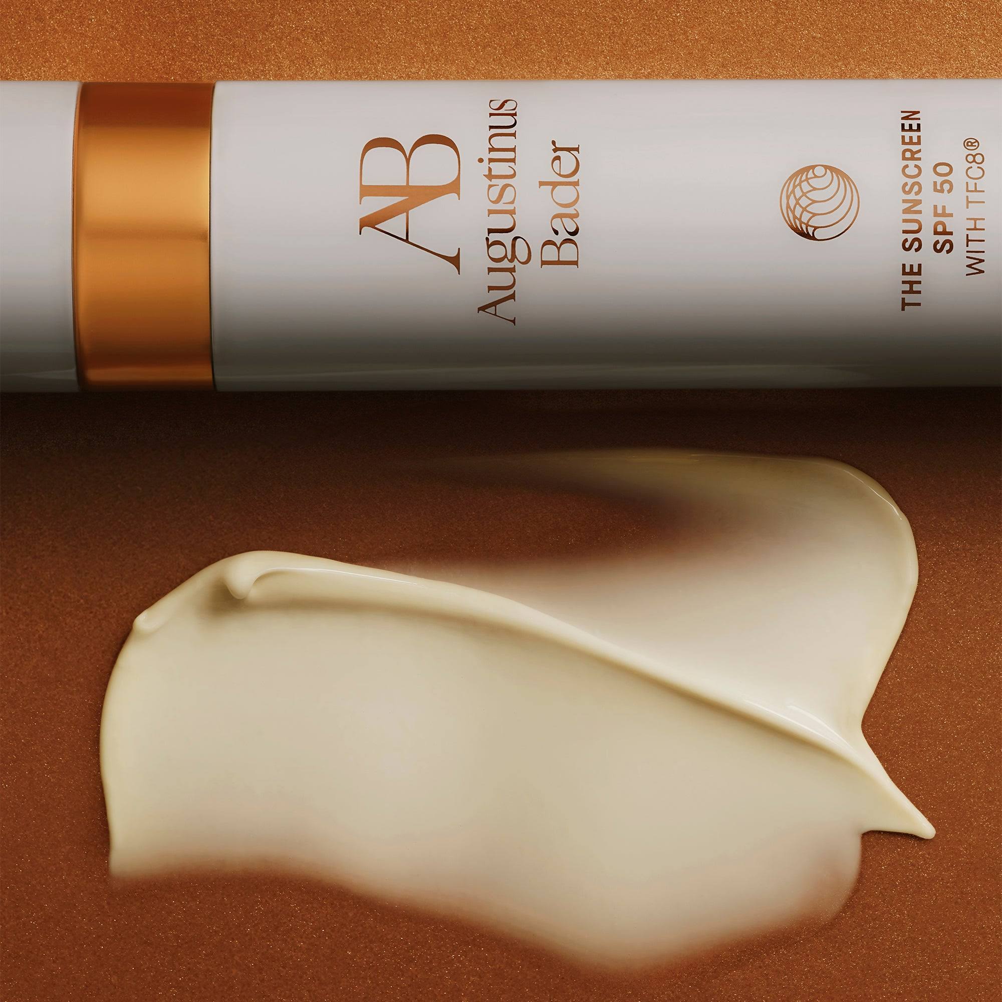 Augustinus Bader sunscreen tube with a swatch of cream on a brown background