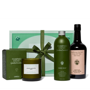 Flamingo Estate garden essentials including a candle, soap, and olive oil bottle on a white background.