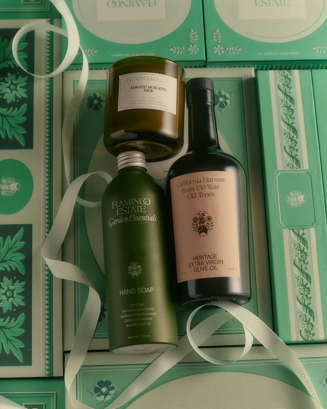 Flamingo Estate garden essentials including a candle, soap, and olive oil bottle on a white background.