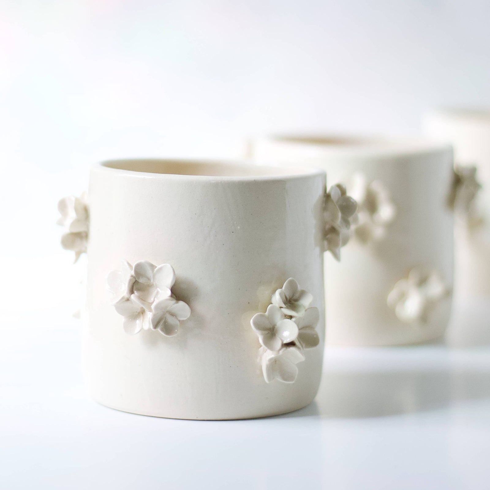 A hand-made cream clay ceramic vase with clusters of sculpted cream-colored ceramic flowers on a white background.