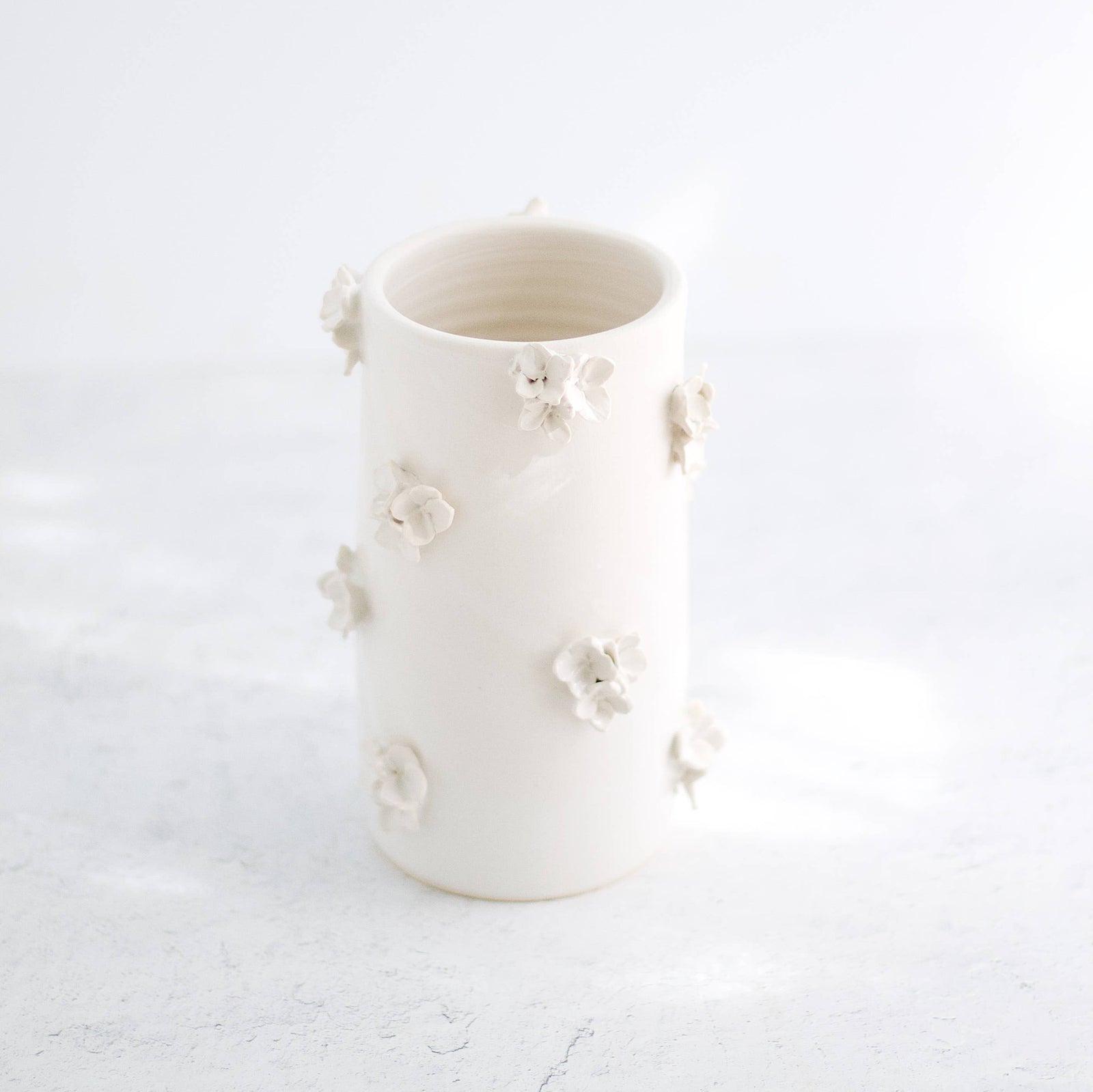 A hand-made cream clay ceramic vase with clusters of sculpted cream-colored ceramic flowers on a white background.