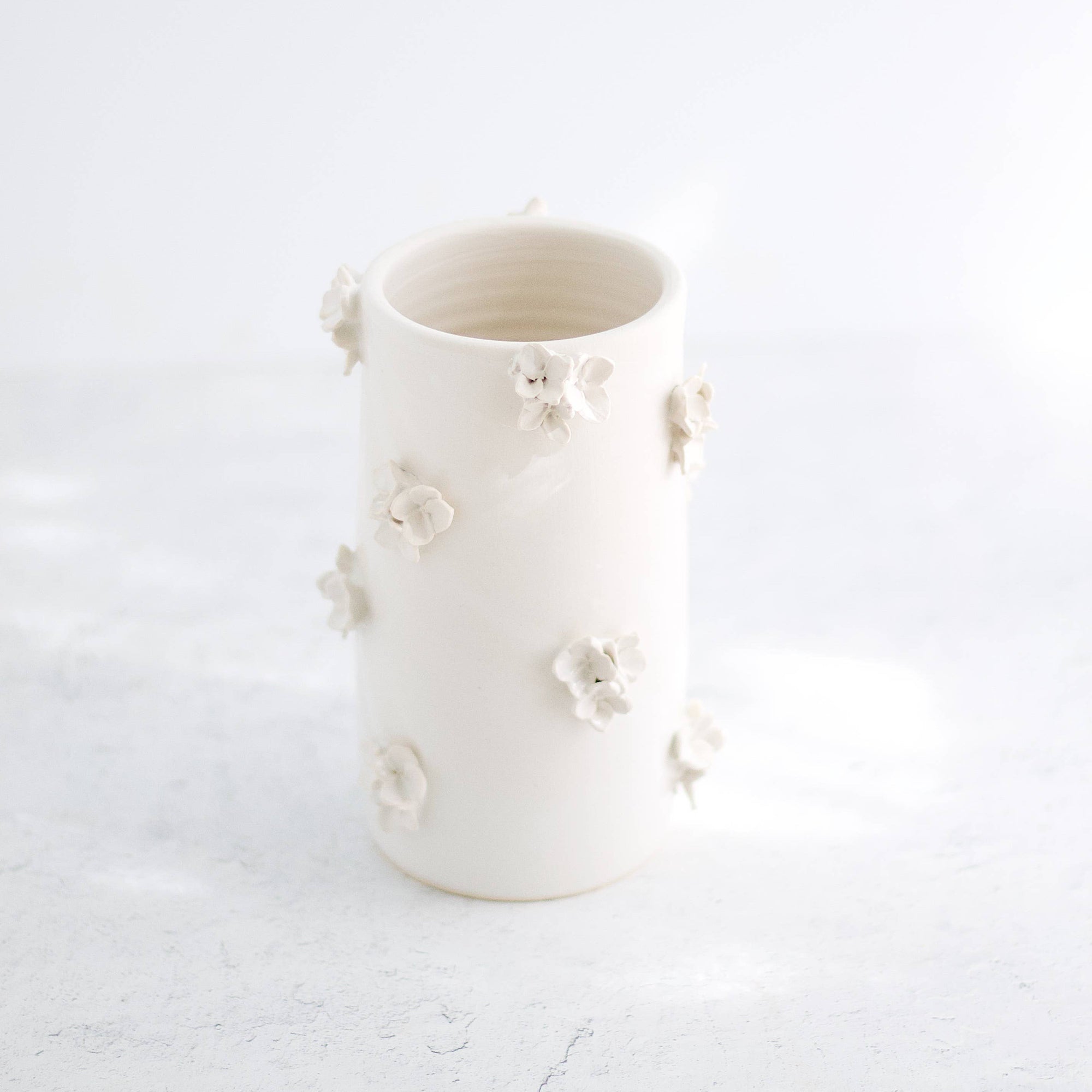 A hand-made cream clay ceramic vase with clusters of sculpted cream-colored ceramic flowers on a white background.