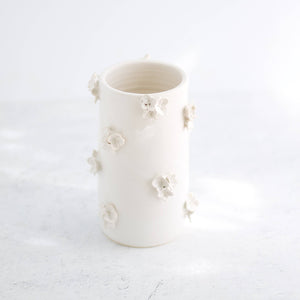 A hand-made cream clay ceramic vase with clusters of sculpted cream-colored ceramic flowers on a white background.