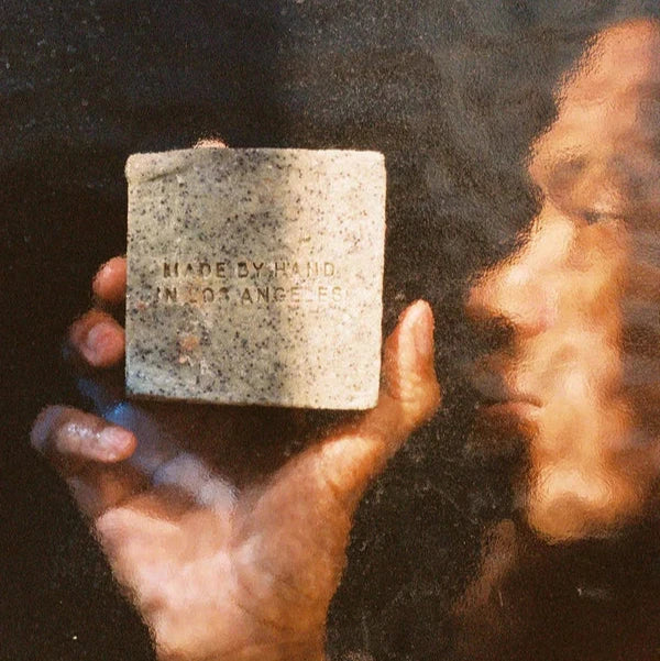 A person holding a bar of morning exfoliating soap, hand made in Los Angeles by Flamingo Estate