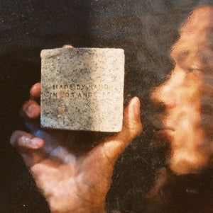 A person holding a bar of morning exfoliating soap, hand made in Los Angeles by Flamingo Estate