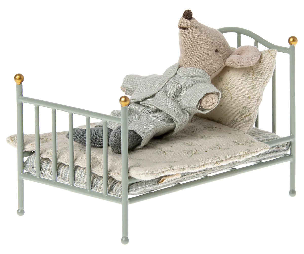 Small mouse toy in a miniature bed with a blanket.