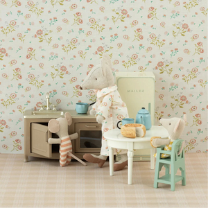 Children's play kitchen set with toys against a floral wallpapered wall.