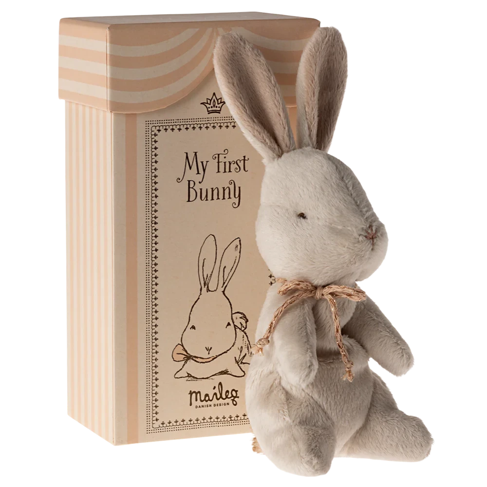 A small plush bunny toy with a beige ribbon around its neck, sitting inside a beige gift box with 'My First Bunny' written on the lid.