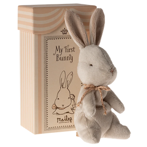 A small plush bunny toy with a beige ribbon around its neck, sitting inside a beige gift box with 'My First Bunny' written on the lid.