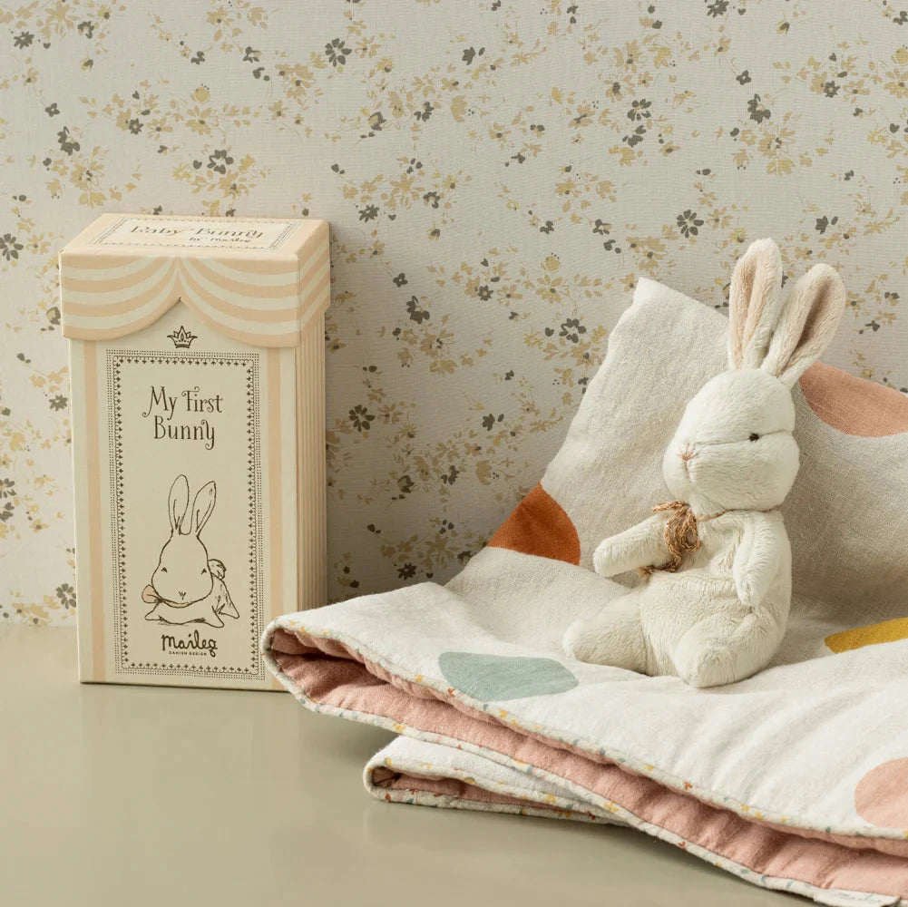 A small plush bunny toy with a beige ribbon around its neck, sitting inside a beige gift box with 'My First Bunny' written on the lid.
