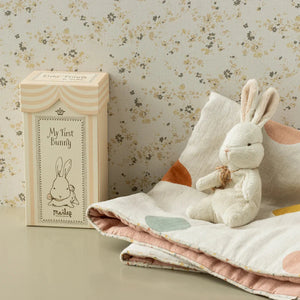 White plush bunny toy with a wooden box labeled 'My first bunny' on a floral-patterned background.