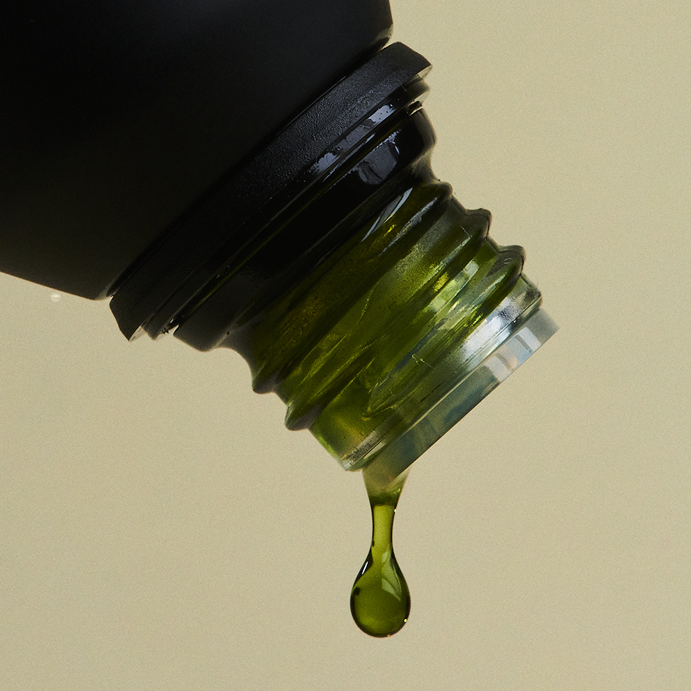 Close-up of a dropper bottle with green liquid dripping against a beige background