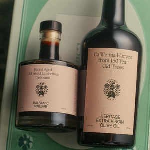 A bottle of balsamic vinegar and extra virgin olive oil atop a green decorative box. 