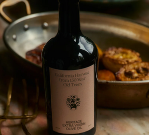 A bottle of olive oil in front of a pan of food. 
