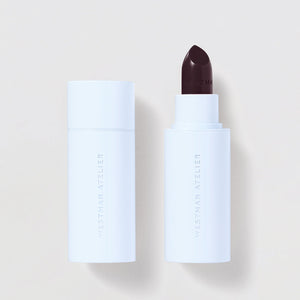 White cosmetic tube with a dark brown applicator on a light beige background