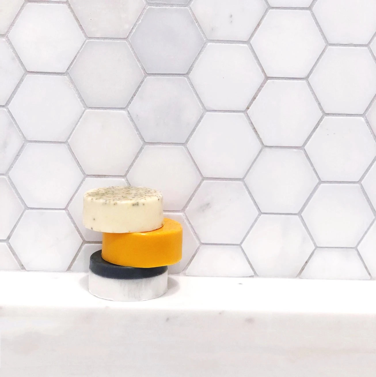 Stack of colorful soap bars on a white surface with a hexagonal tile backsplash.