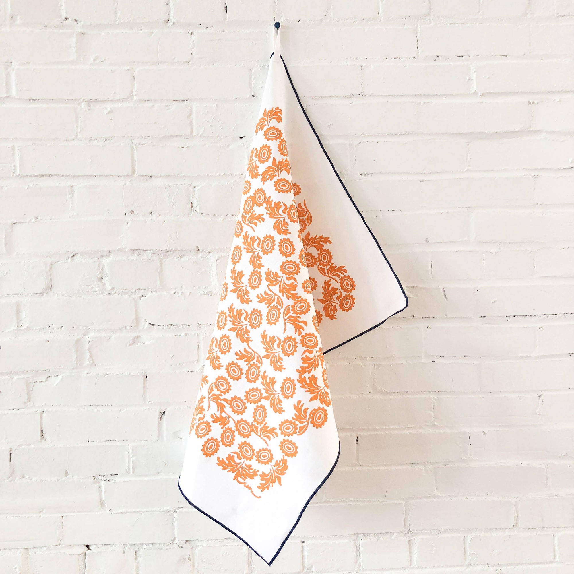 White towel with orange floral pattern hanging against a white brick wall
