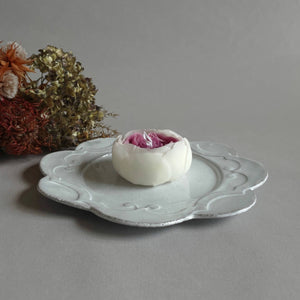 A white and pink peony candle on a white saucer. 