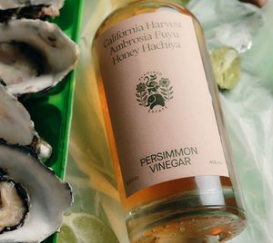 A bottle of persimmon vinegar next to oysters in the shell. 