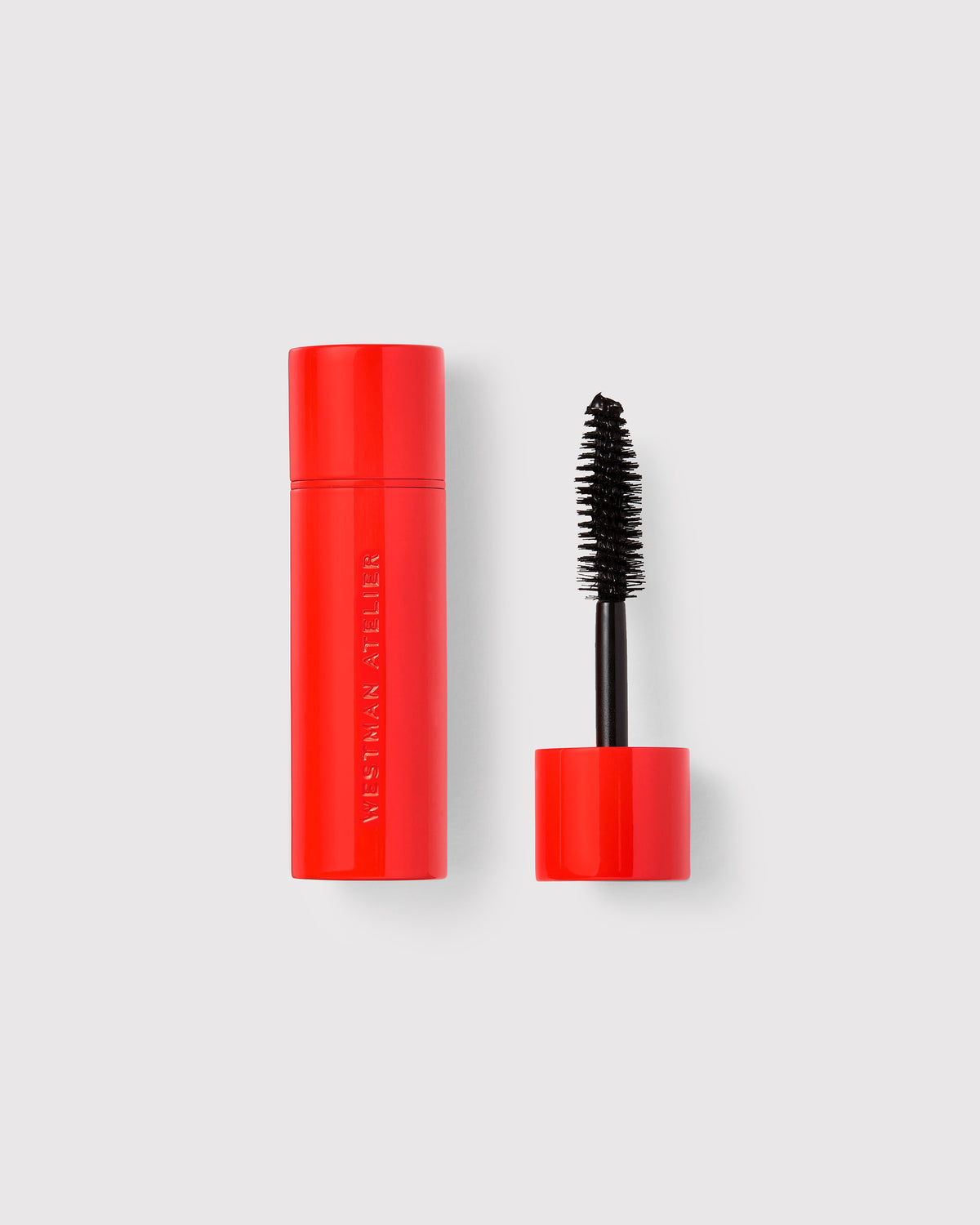 A red mascara tube with the cap off, showing the wand with bristles coated in black mascara.
