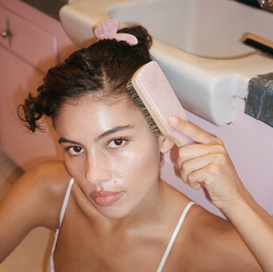 A woman with dark hair using the Emijay mini boar bristle hair brush in Pink Sugar