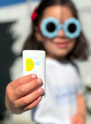 Child holding a tube of Play sunscreen with a blurred background