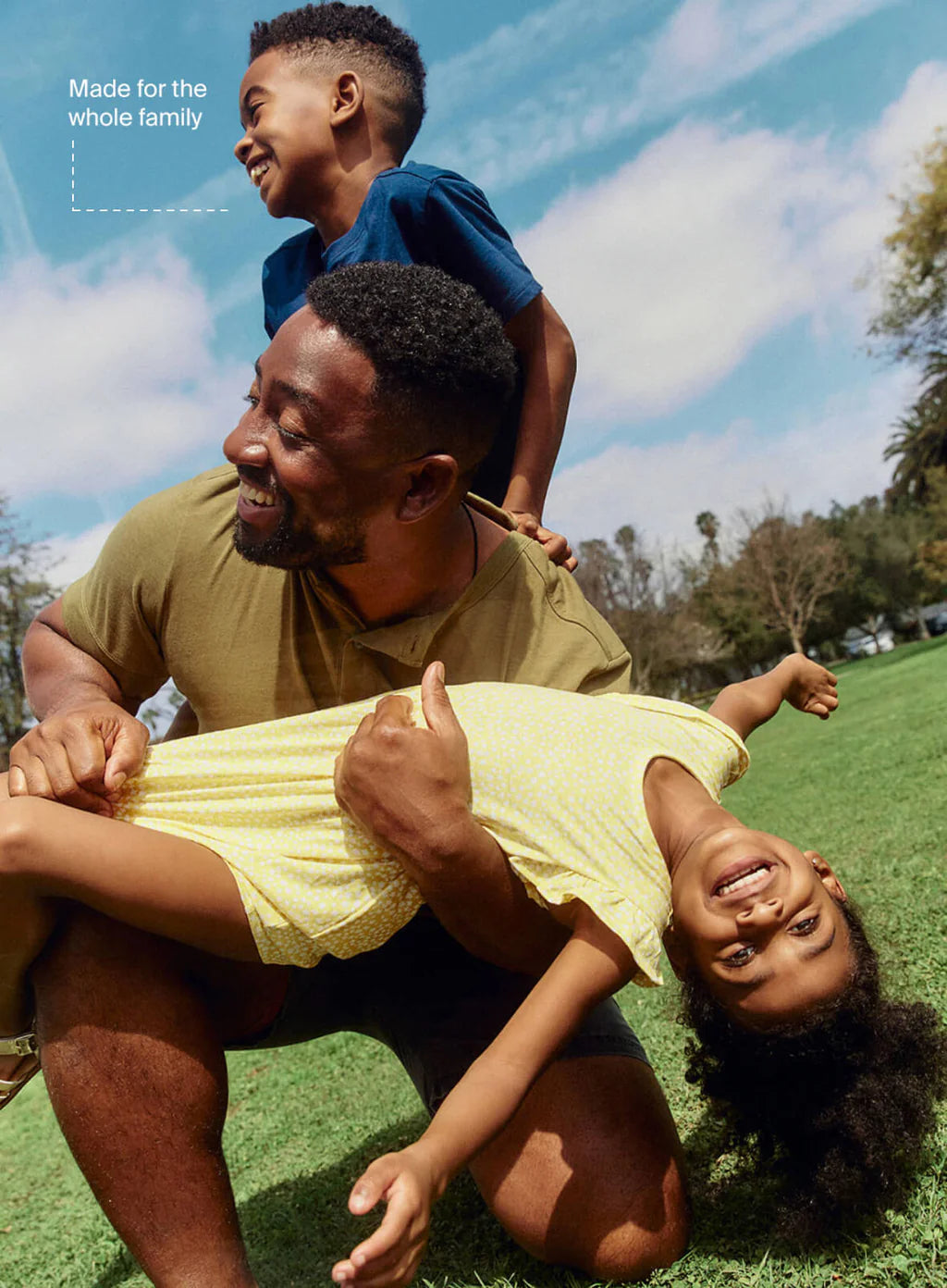 Man playing with two children on a grassy field with a blue sky.