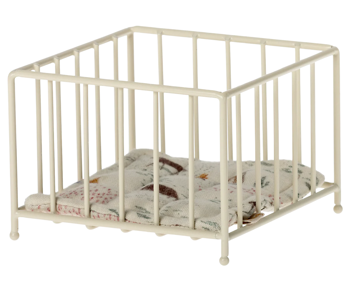 A small, beige-colored metal playpen with a cushion inside, designed for doll-sized figures.