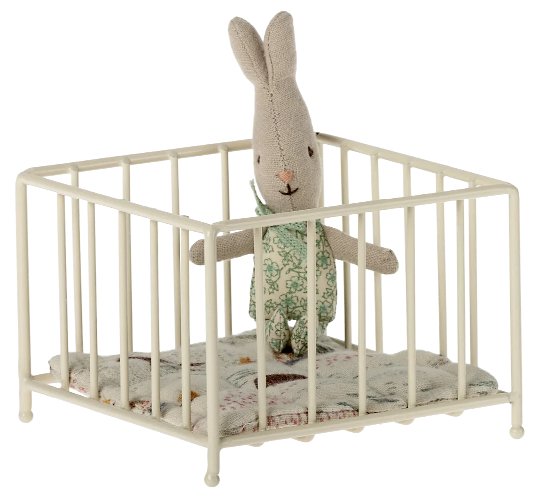 A small, beige-colored metal playpen with a cushion inside, designed for doll-sized figures.