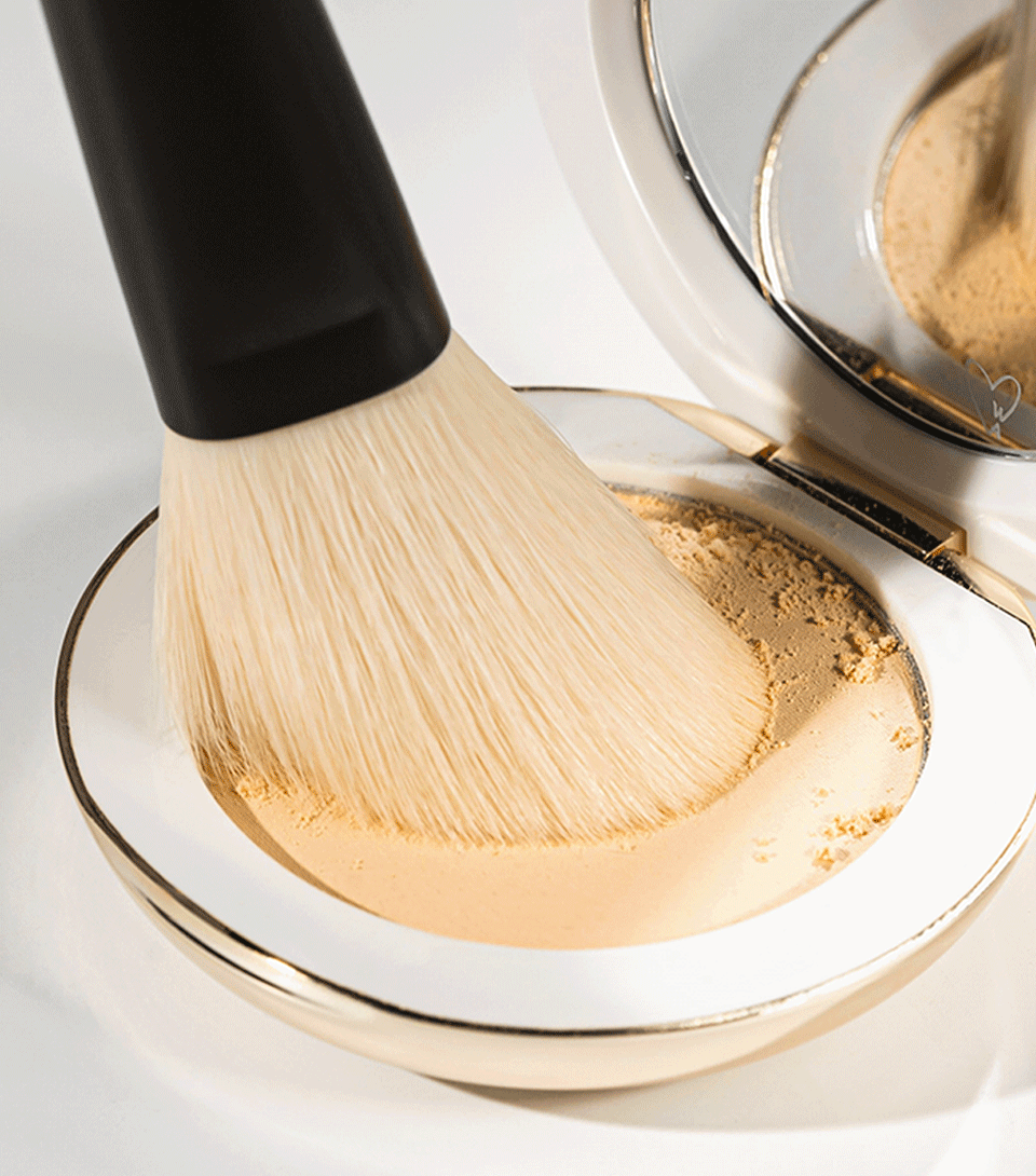 An oval-shaped powder brush with a black handle and beige bristles, designed for precise application of powder products.