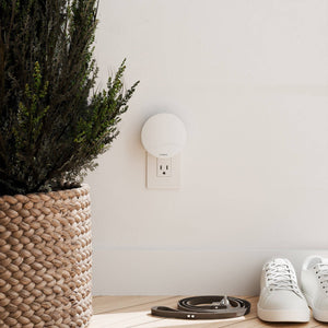 A Vitruvi Push plugin wall diffuser on a white wall with a plant and sneakers nearby