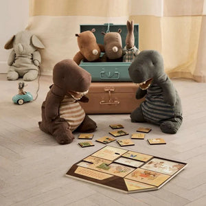 Plush toy animals around a suitcase with a board game on a wooden floor.