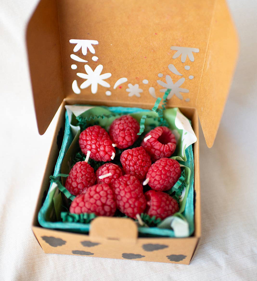 A set of raspberry candles, in a green paper produce box