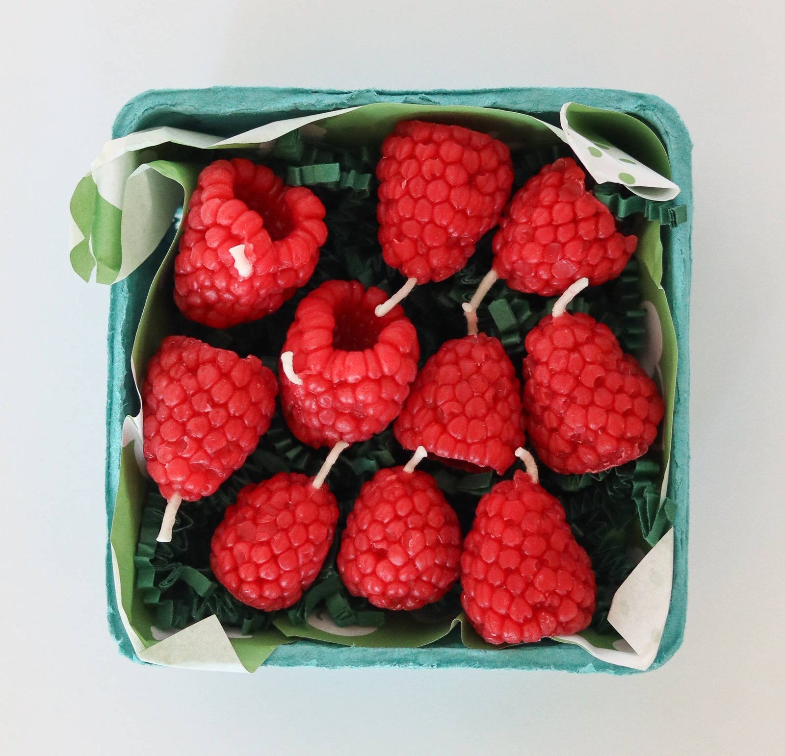 A set of raspberry candles, in a green paper produce box