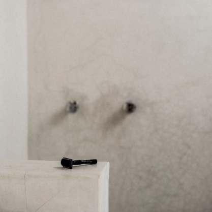A black well kept razor on the edge of a shower stall. 