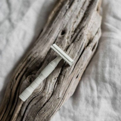 White safety razor on a piece of driftwood with a soft, neutral background