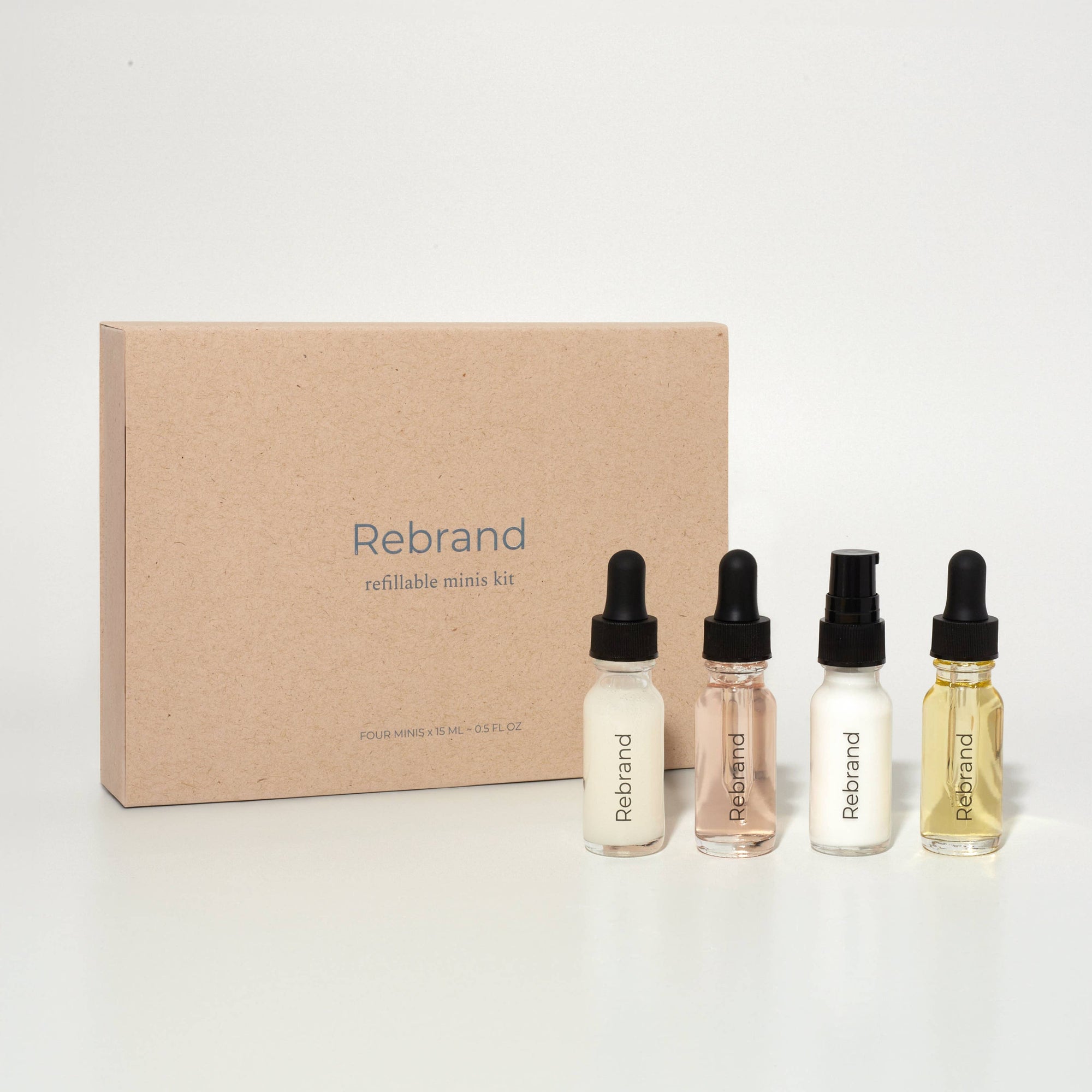 A collection of four 15 ML glass bottles with dropper caps, labeled Dream Cleanser, Power Serum, Day & Night Cream, and Super Oil, positioned in front of a brown cardboard box with the brand name Rebrand visible.