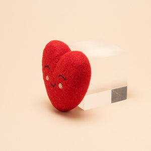 A wool felt heart shaped dog toy, with a smile and eyes embroidered on it