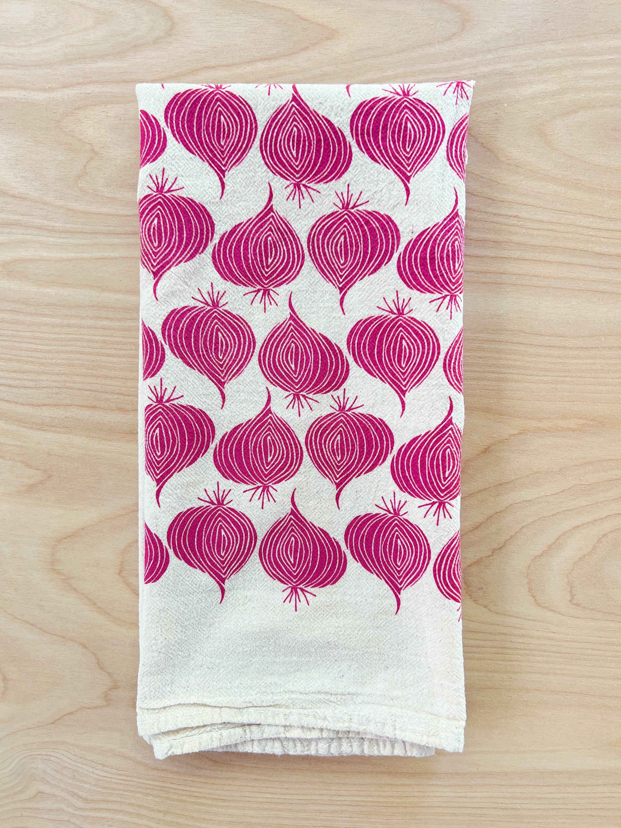 The Noon Designs red onion tea towel is white with bright red onions printed on it. 