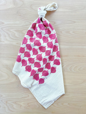 The Noon Designs red onion tea towel is white with bright red onions printed on it. 