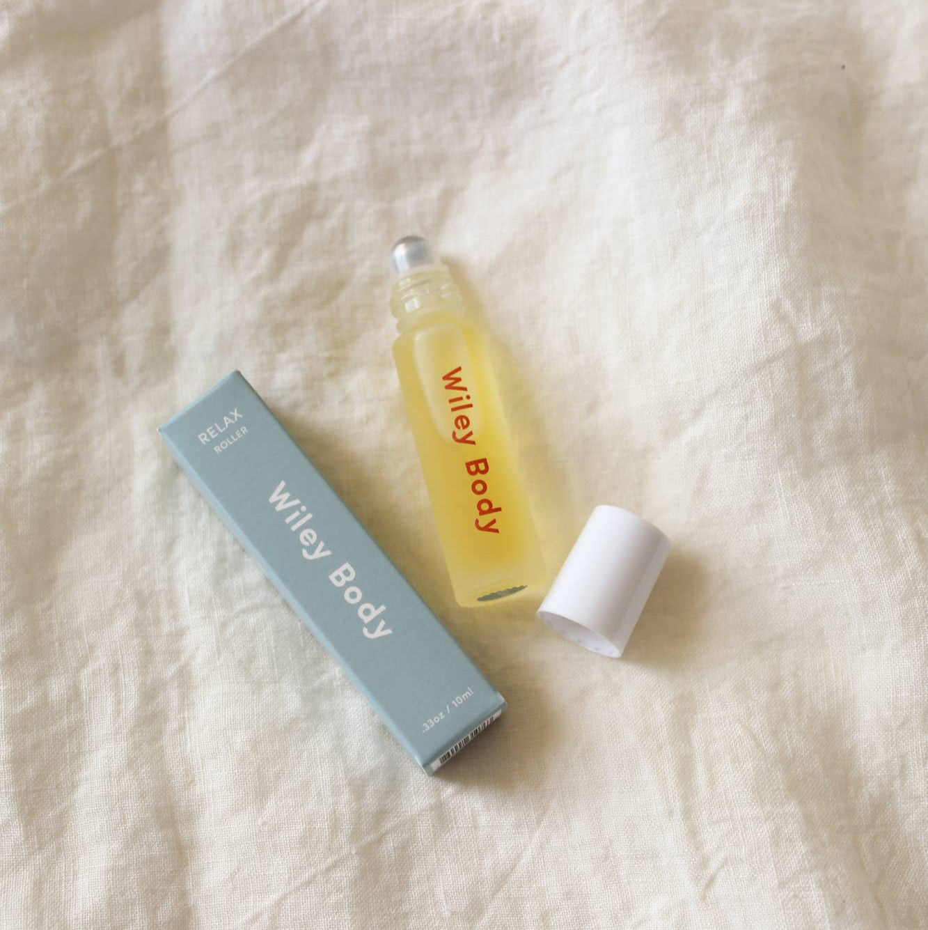 A Relax rollerball next to a blue box on a cream colored piece of fabric. 