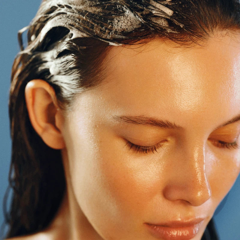 Close-up of a woman with her eyes closed, with shampoo in her hair.