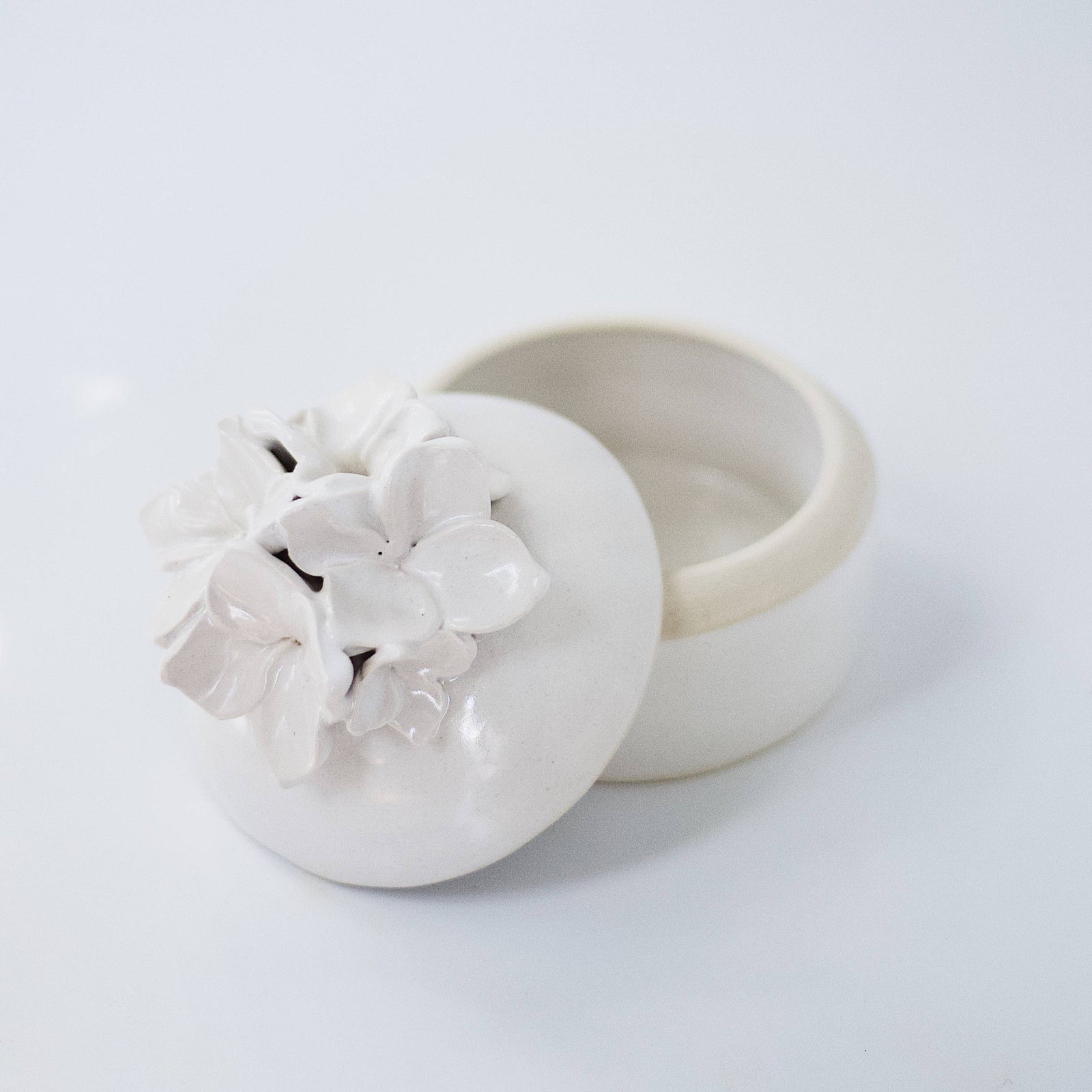 A cream-colored lidded jar with hand-sculpted flowers attached to the lid, placed on a white background.