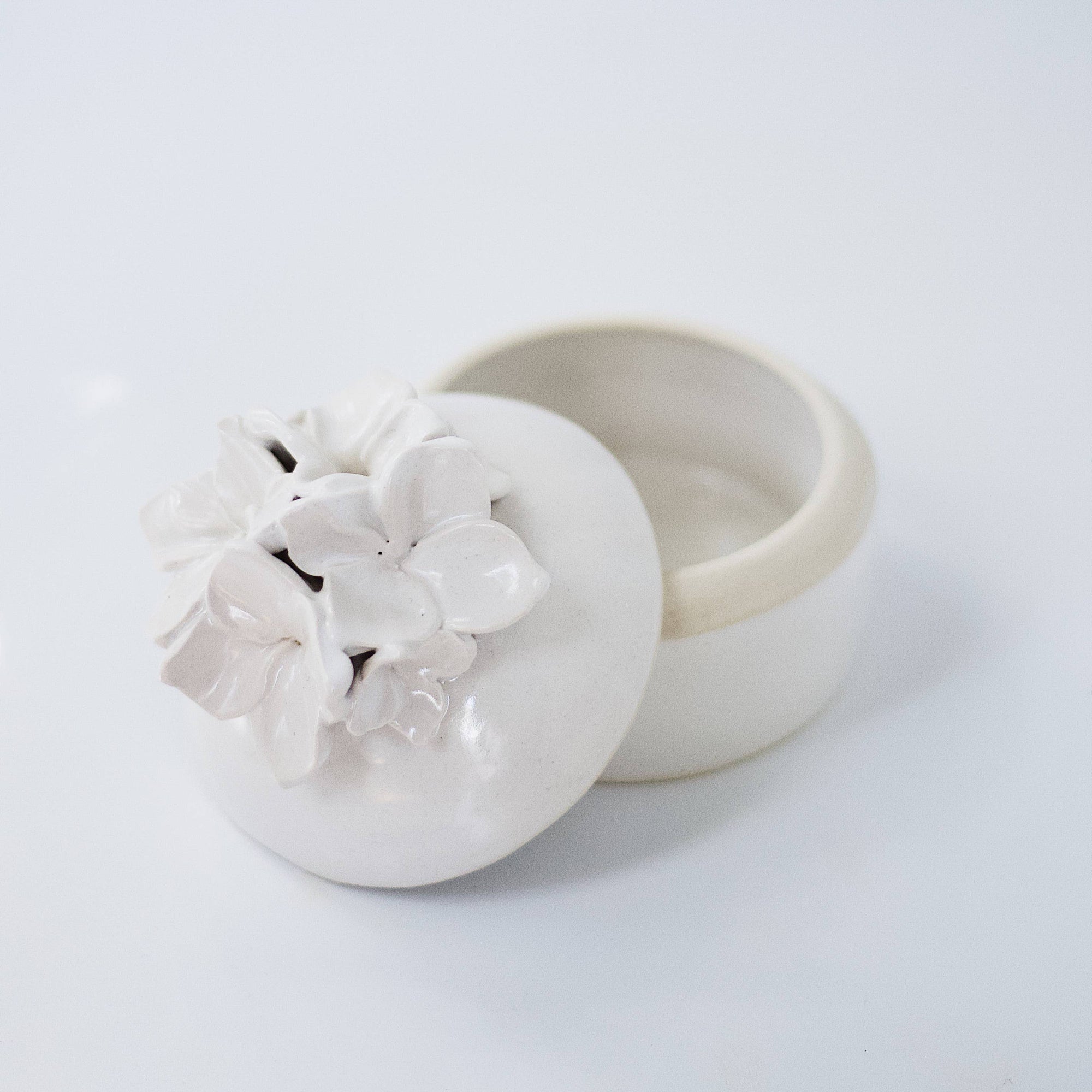A cream-colored lidded jar with hand-sculpted flowers attached to the lid, placed on a white background.