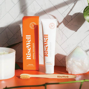 A tube of rise well toothpaste next to an orange box on an orange counter, with a toothbrush nearby
