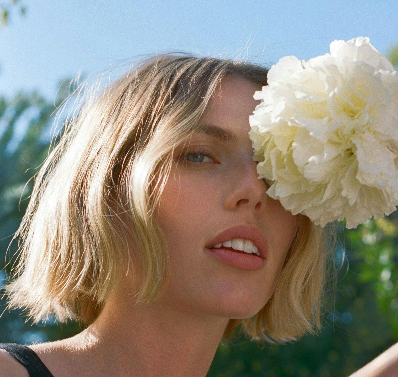 A bottle of Rūz Air Thickening Spray with its packaging box, both featuring a floral pattern. The bottle has a pink spray nozzle and the packaging is white with pink accents.