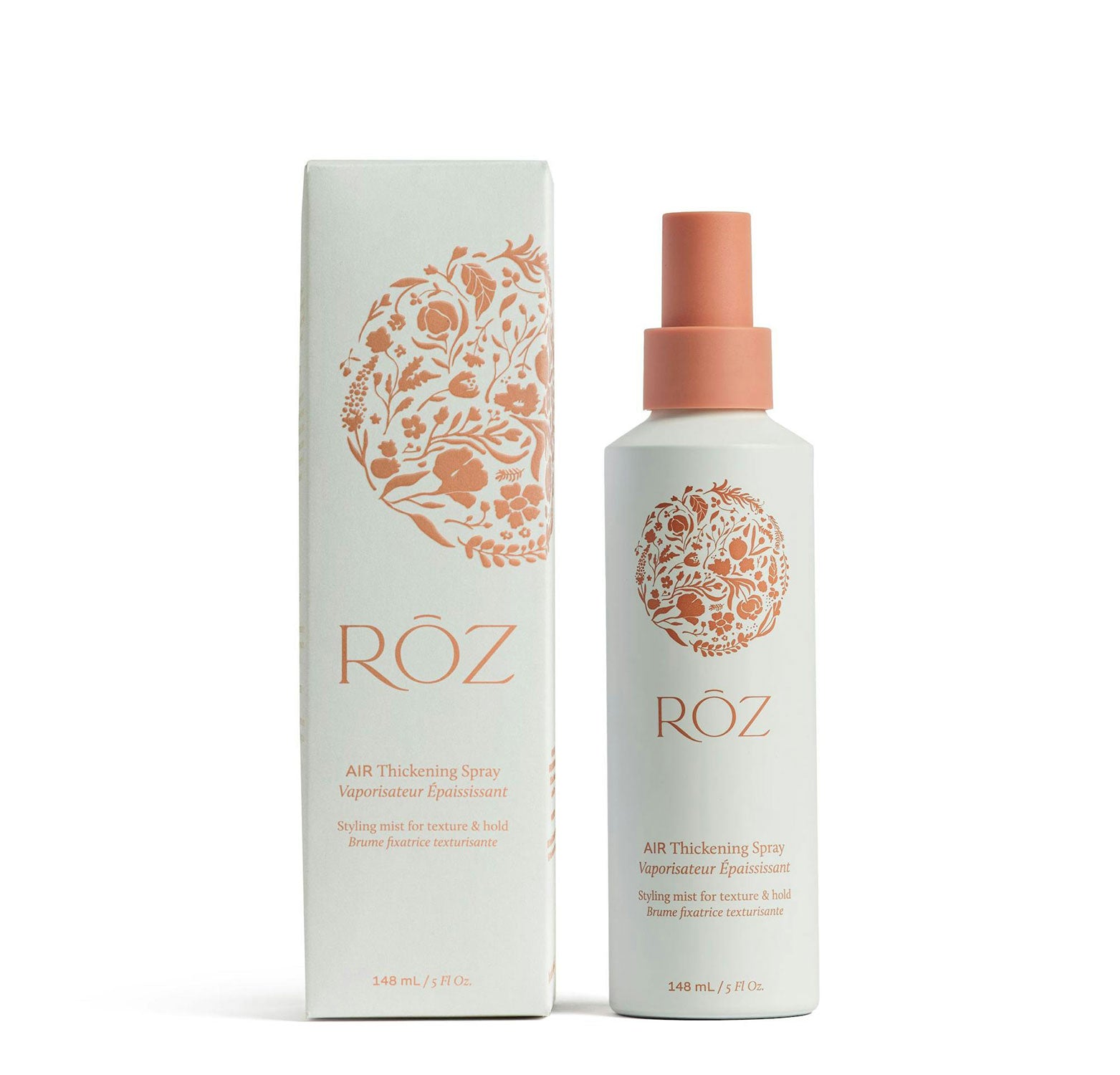 A bottle of Rūz Air Thickening Spray with its packaging box, both featuring a floral pattern. The bottle has a pink spray nozzle and the packaging is white with pink accents.