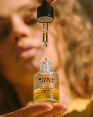 Bottle of Wonder Valley Rosemary Hair Oil with a dropper being held above it.
